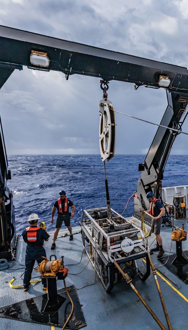 Crew on the back deck of a research vessel recovering a towed camera system in heavy seas